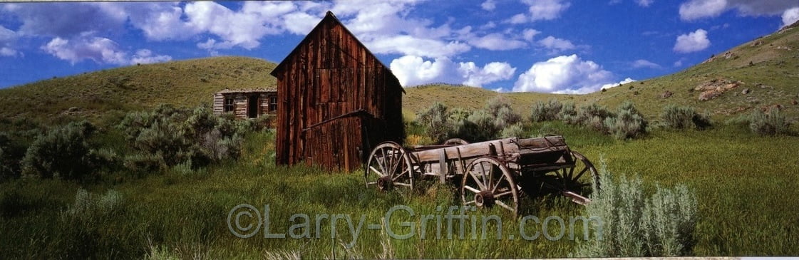 Panoramic photograph of a weathered wooden cabin and an old farm wagon in sagebrush hills