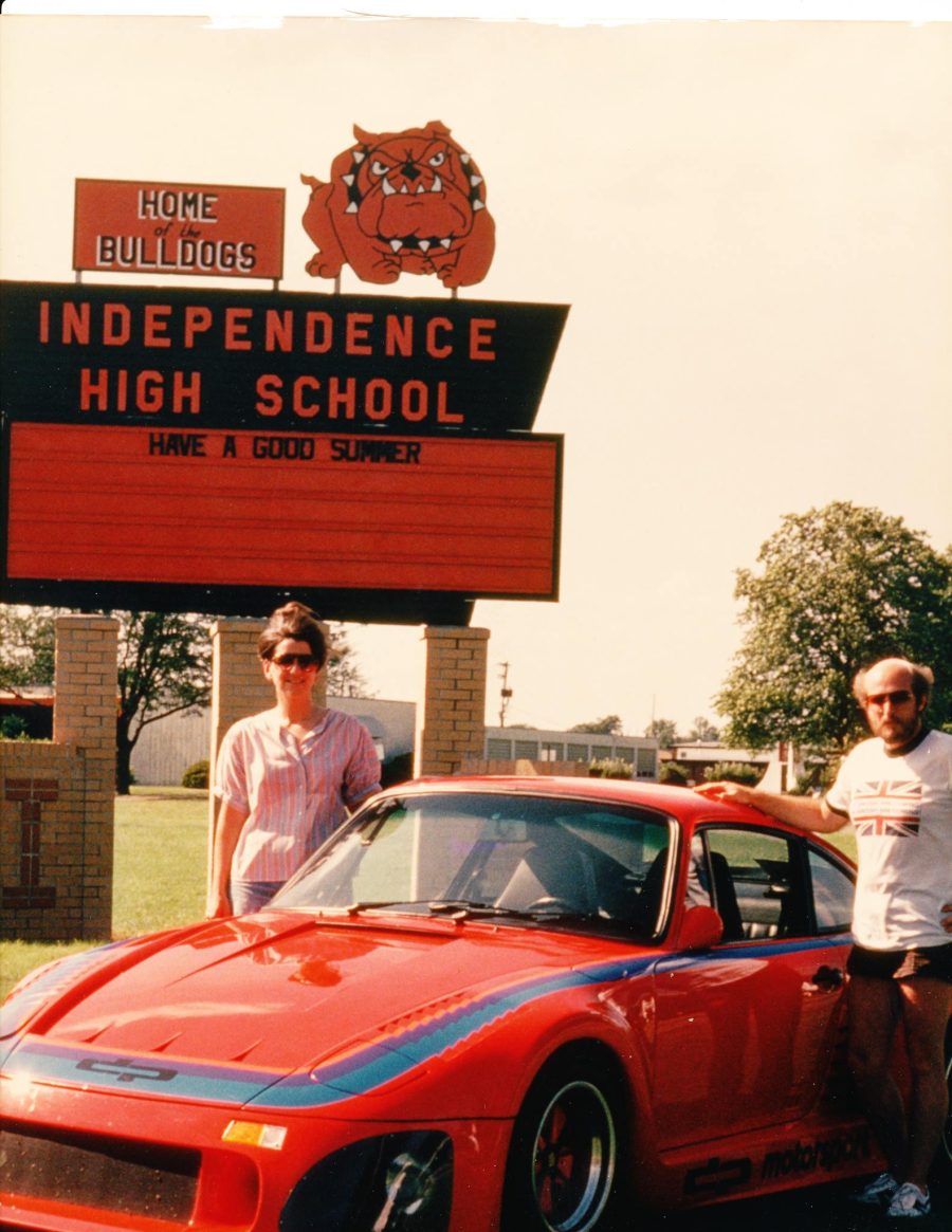 Larry Griffin and a classmate beside his red Porsche 935 in front of the Independence High School sign