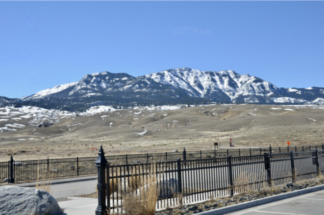 A snow-covered mountain ridge rising beyond a black iron fence