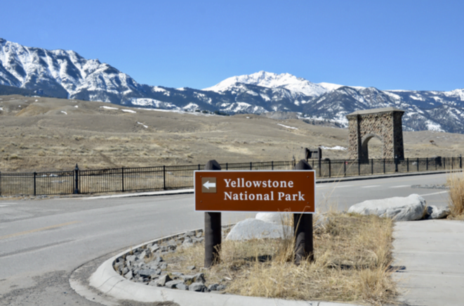 Yellowstone National Park sign and the Roosevelt Arch under snowy peaks
