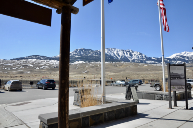 Snow-covered mountains seen past flagpoles from a covered porch